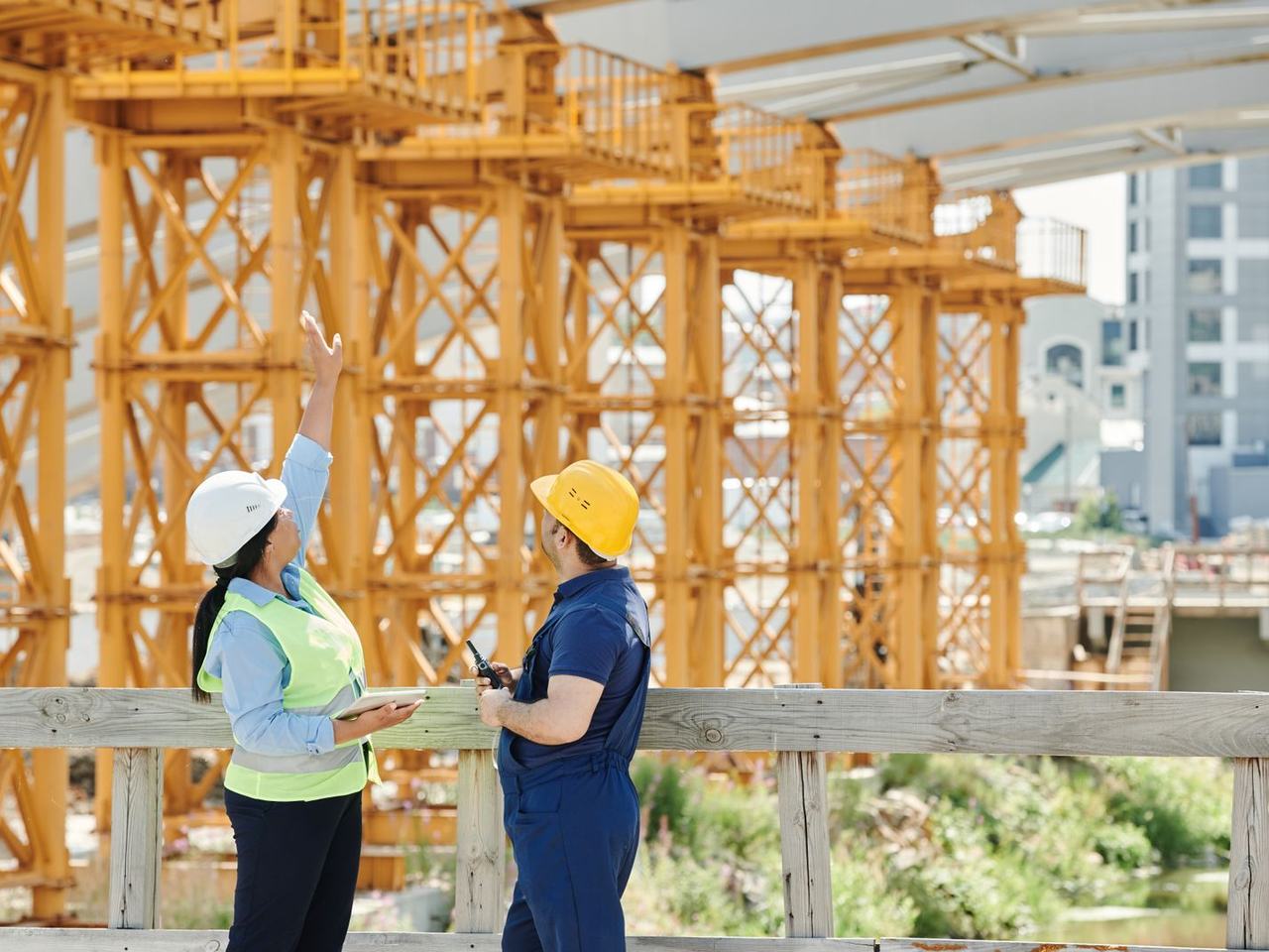 Two engineers in hard hats reviewing a site together, one holding a tablet